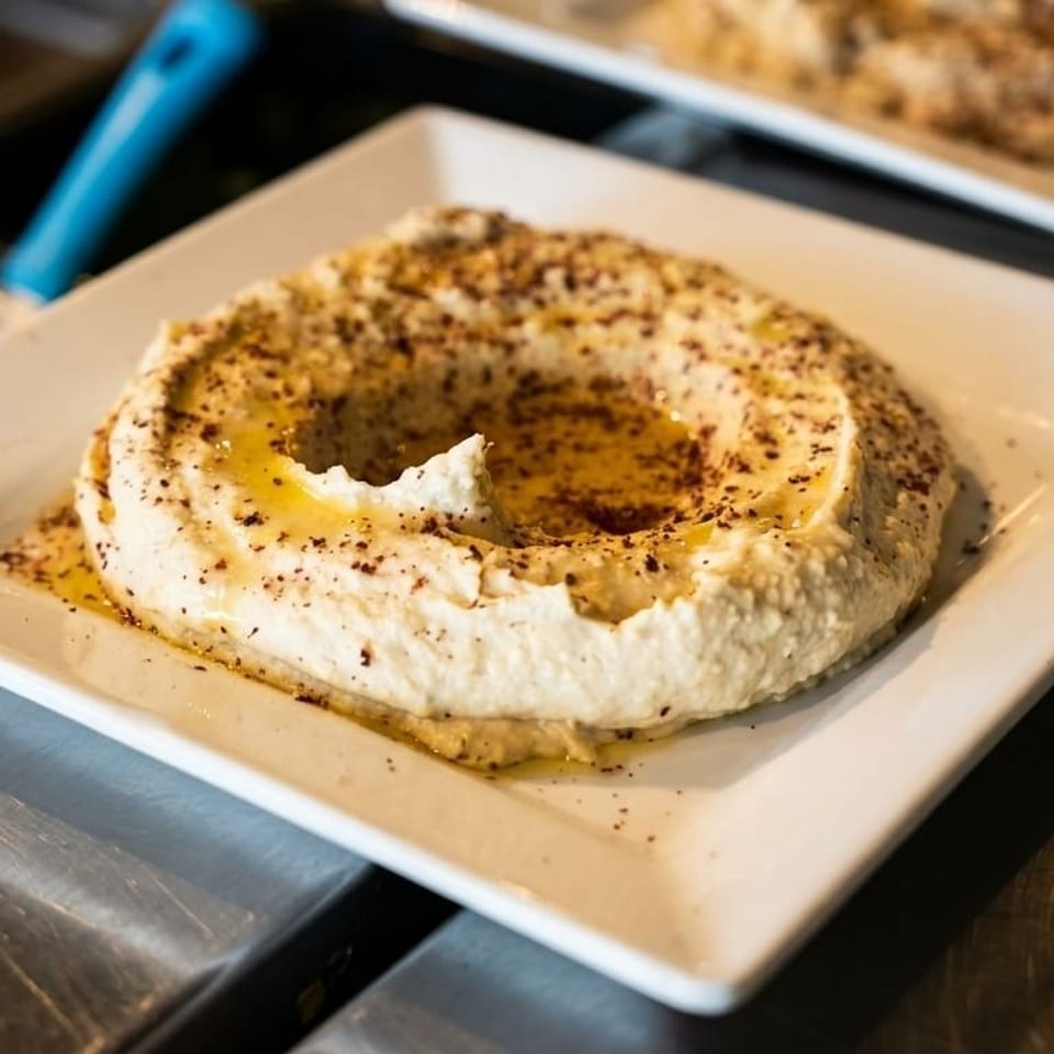 Creamy hummus with olive oil and spices, served on a white square plate.