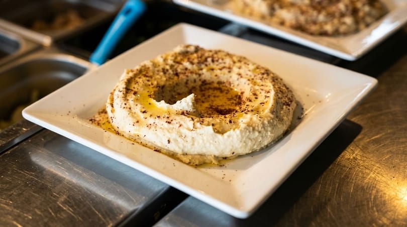 Creamy hummus with olive oil and spices, served on a white square plate.