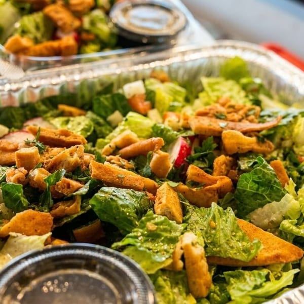 Large catering tray of fresh green salad with croutons, radishes, and dressing cups.