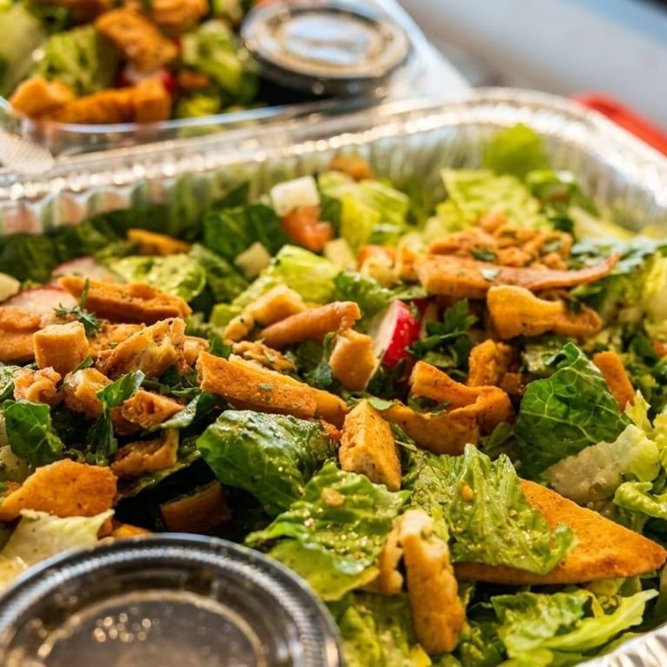 Large catering tray of fresh green salad with croutons, radishes, and dressing cups.