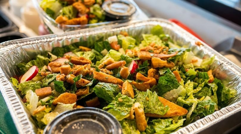 Large catering tray of fresh green salad with croutons, radishes, and dressing cups.