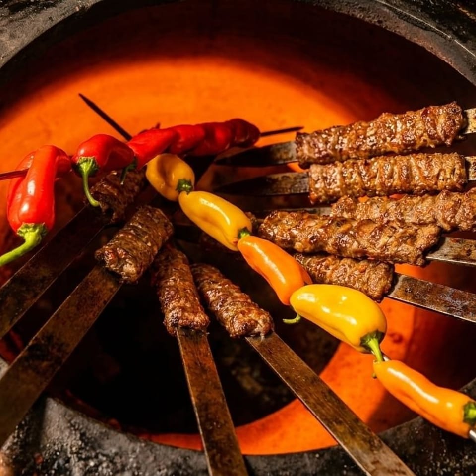 Skewers of meat and colorful peppers cooking inside a glowing tandoor oven.